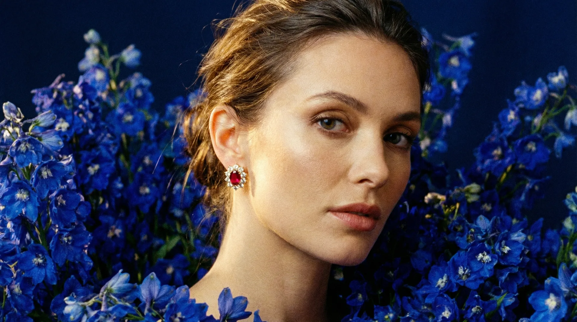 Model wearing ruby and diamond earrings among blue delphiniums