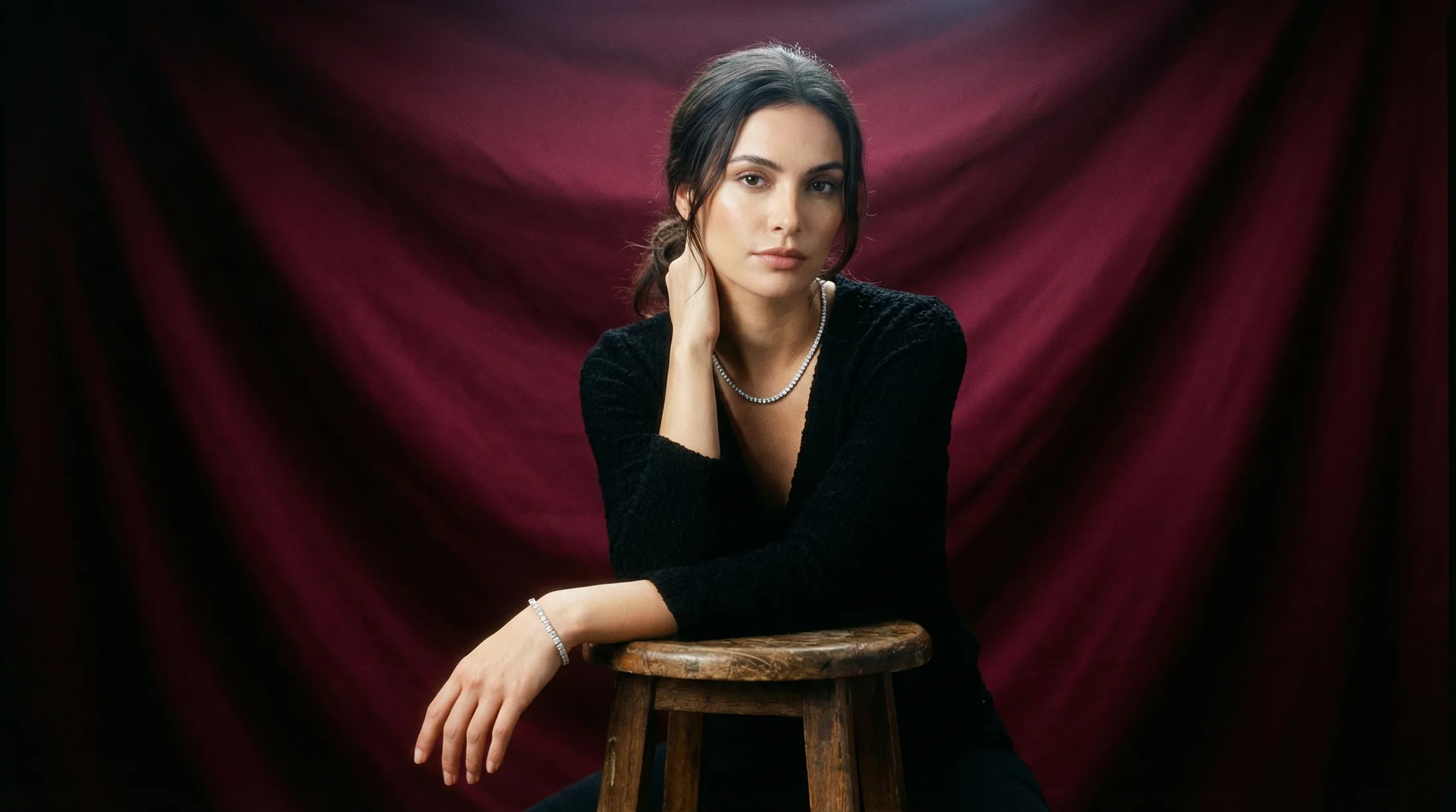 Female model wearing diamond tennis necklace and bracelet against burgundy fabric