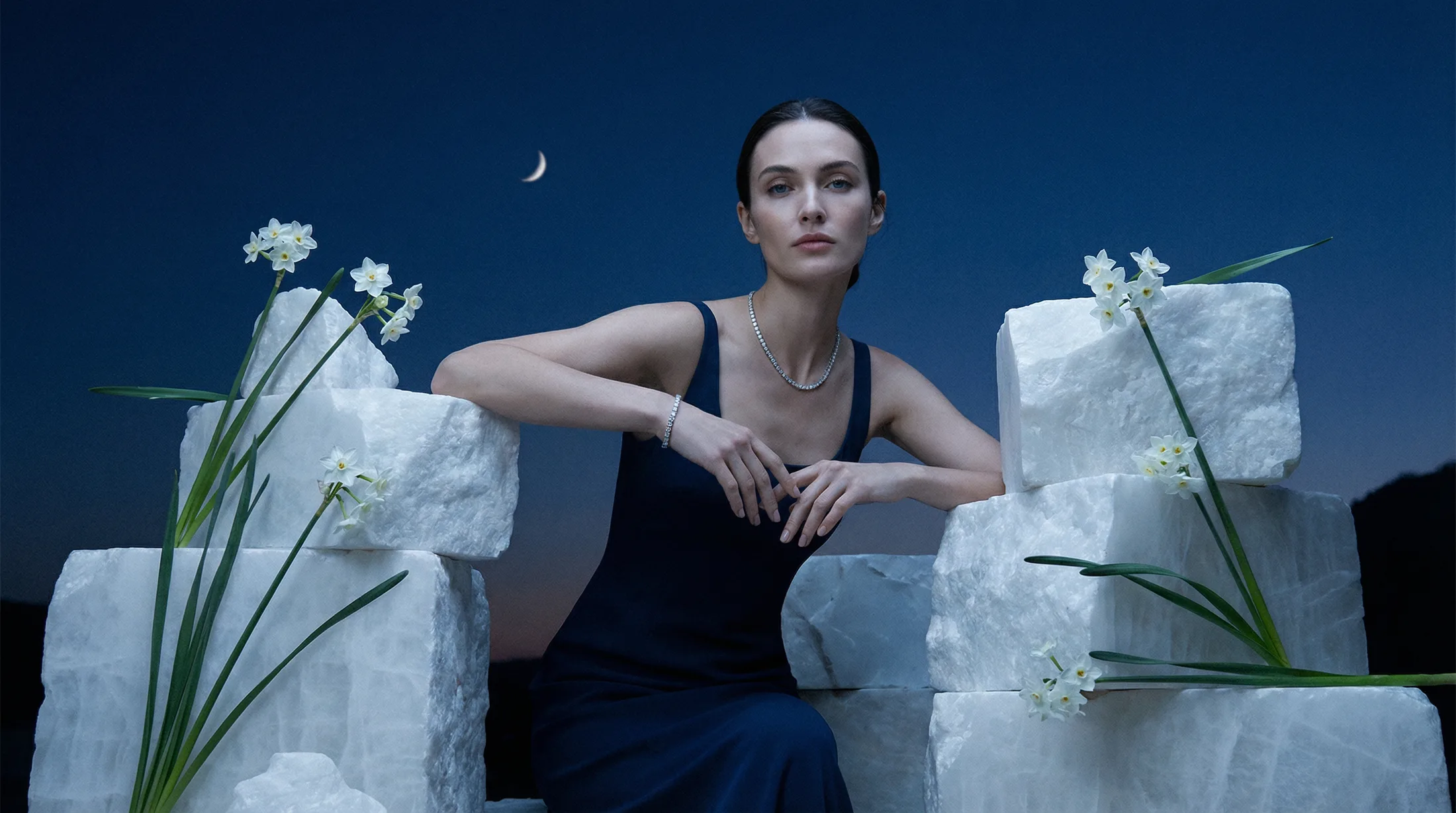 Female model wearing a diamond tennis necklace and bracelet among moonlit stone blocks