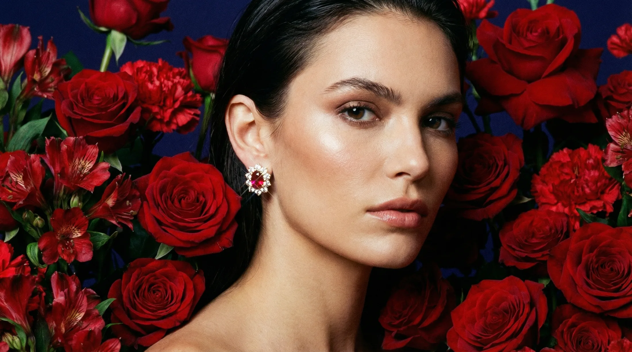 Model wearing ruby and diamond earrings surrounded by red roses